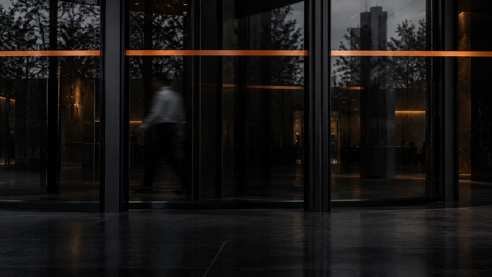 A blurred figure passing through the glass doors of a modern office